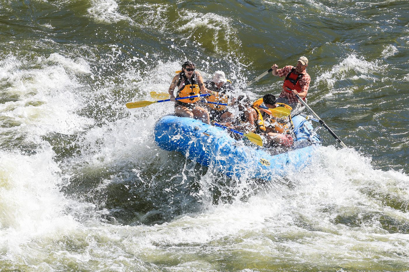 A raft of paddlers punching through a large standing wave, everyone soaked