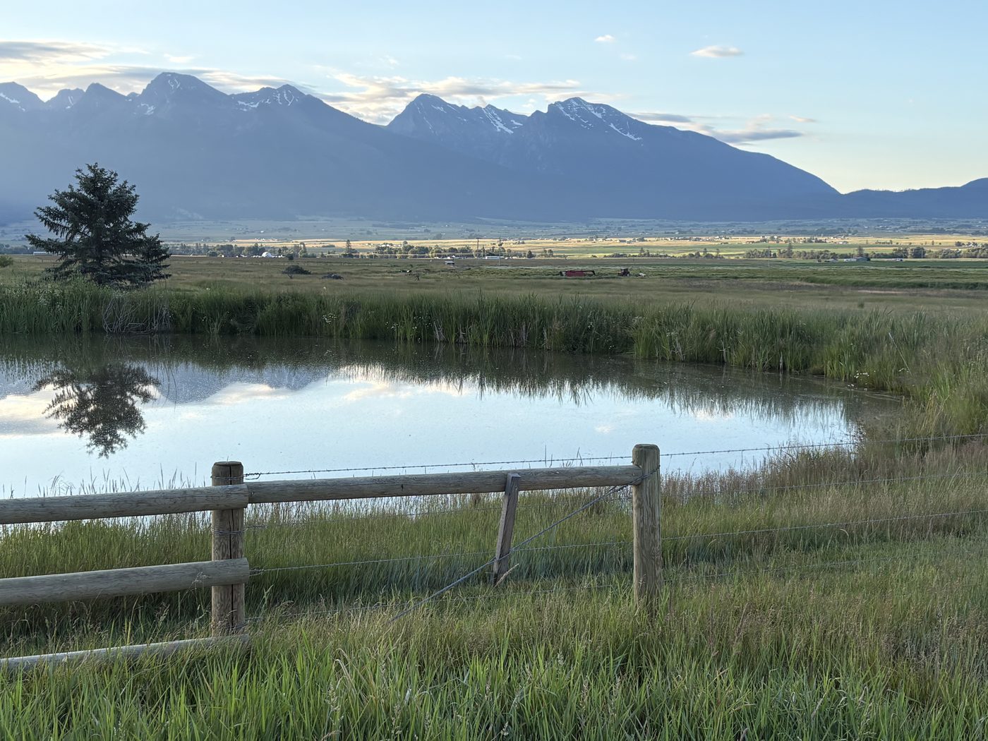 The Mission Mountains rising over flat green fields and a pond