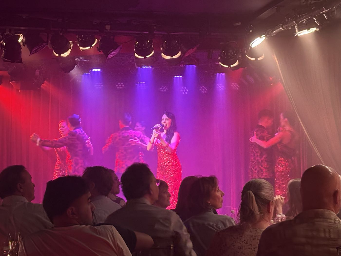 A singer and tango dancers on a stage lit red and purple